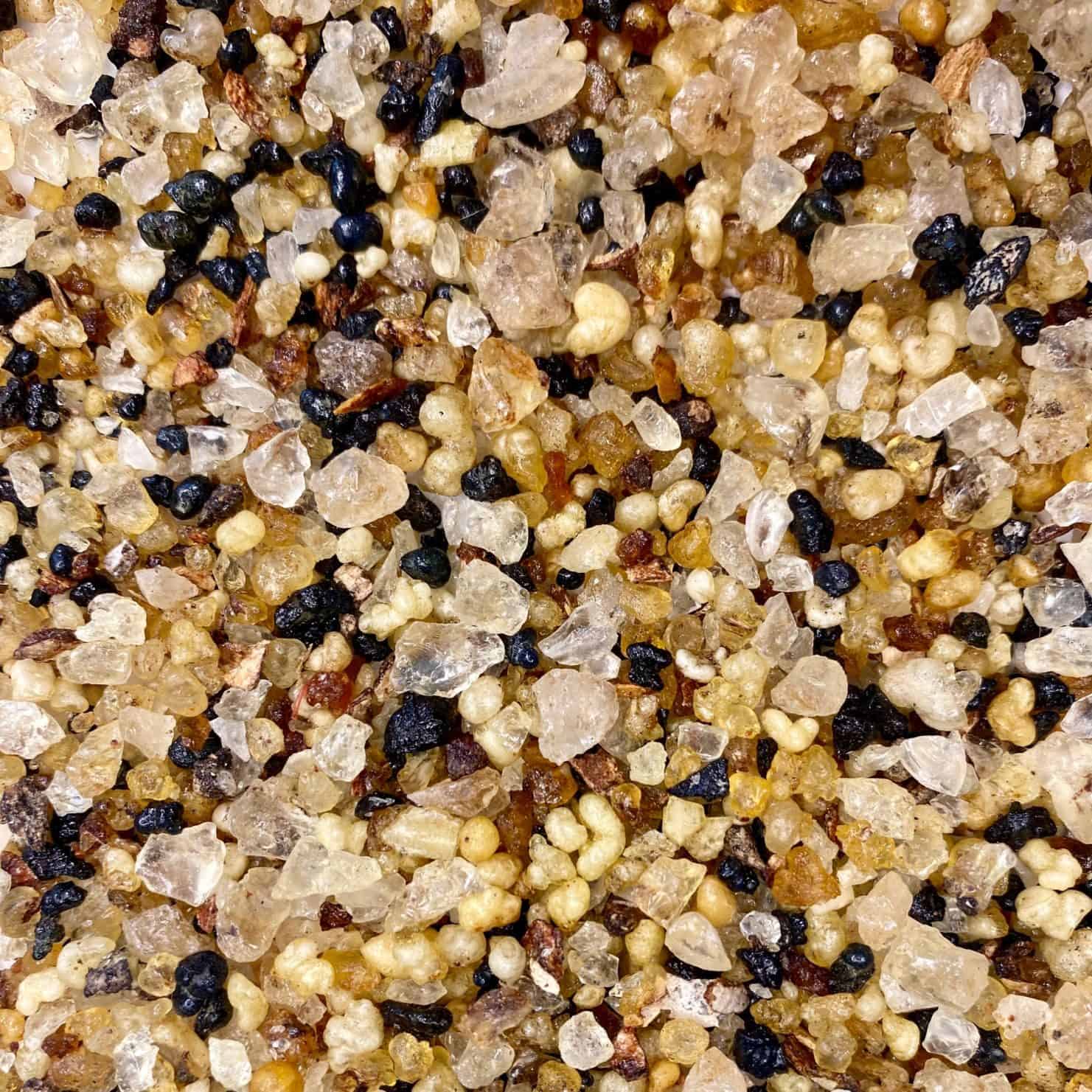 Nahaufnahme einer Mischung verschiedener Harzperlen in den Farben Gold, Bernstein, Schwarz und Weiß in unterschiedlichen Formen und Größen. Darunter befinden sich Stücke des duftenden Weihrauchharzes Basilika.