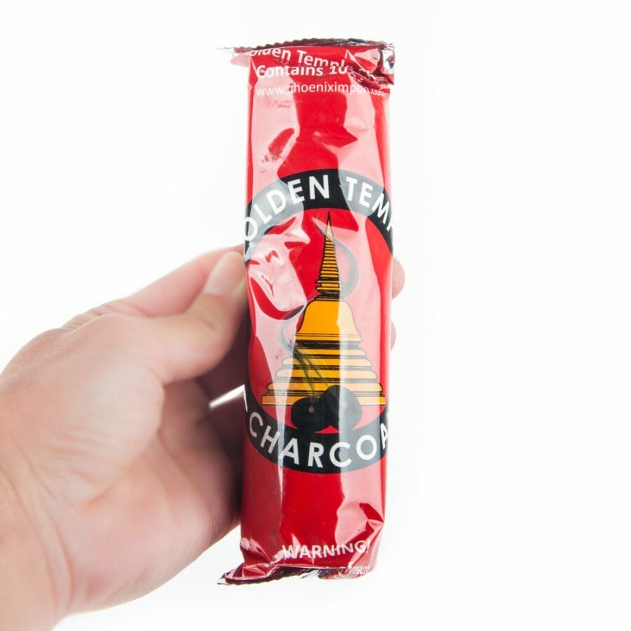 Die Hand einer Person hält eine Packung Holzkohletabletten Golden Temple – 3,3 cm Rotwein-Scotch-Whisky.